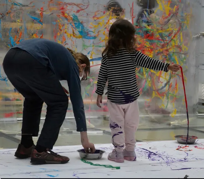 Criança pintando com tinta escorrida sobre uma tela grande, ao lado de uma educadora, no Arte Yellow